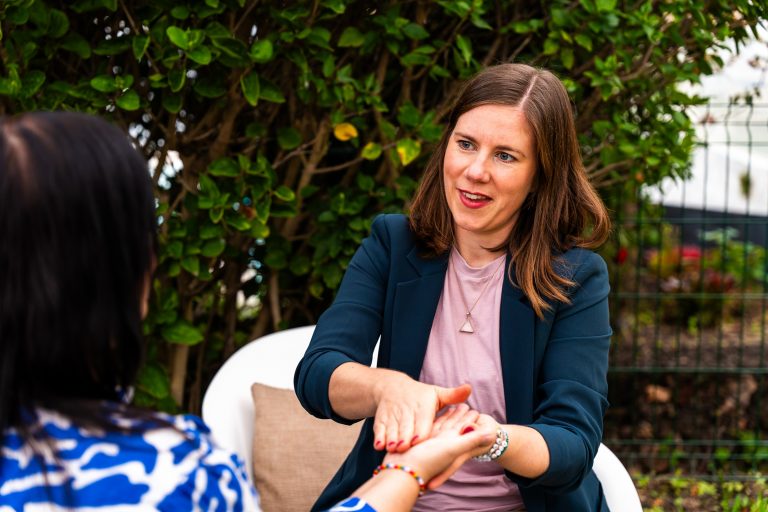 Julia gibt eine Handmassage im Hintergrund grüne Blumenhecke